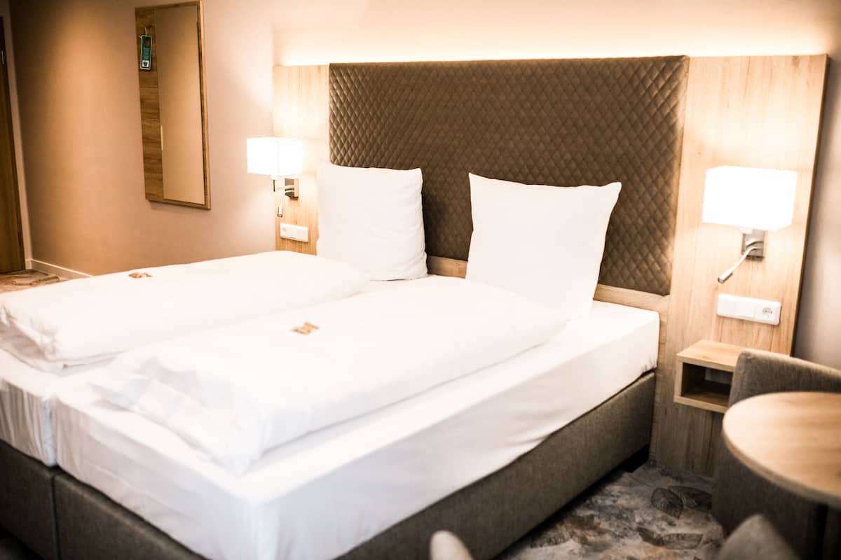 A double bed with white linens, a wooden headboard, bedside lamps, and a small wooden table.
