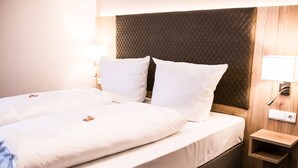A double bed with white linens and two pillows, a wooden headboard, a bedside table with a lamp, and a power outlet. - Wiechmanns Weserhotel (Brake)