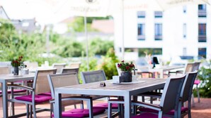 An outdoor seating area with tables and chairs, some with umbrellas, and a building in the background. - Wiechmanns Weserhotel (Brake)