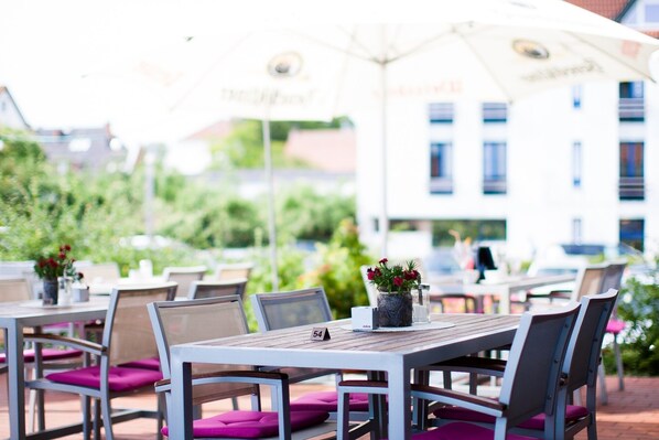 An outdoor seating area with tables and chairs, some with umbrellas, and a building in the background. - Wiechmanns Weserhotel (Brake)
