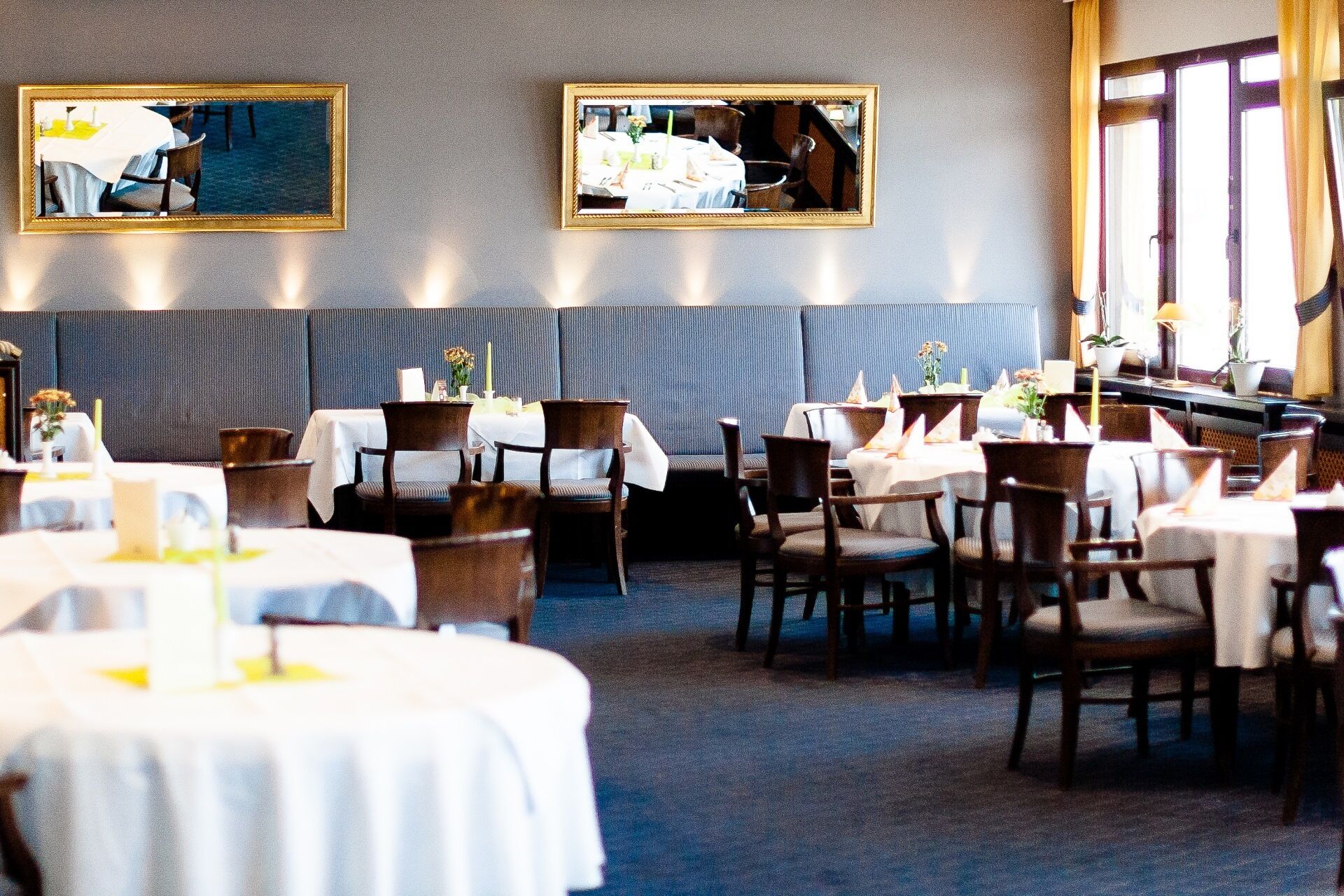 A restaurant with round tables, dark wood chairs, and a grey upholstered bench. There are two framed mirrors on the wall.