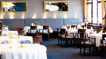 A restaurant with round tables, dark wood chairs, and a grey upholstered bench. There are two framed mirrors on the wall.