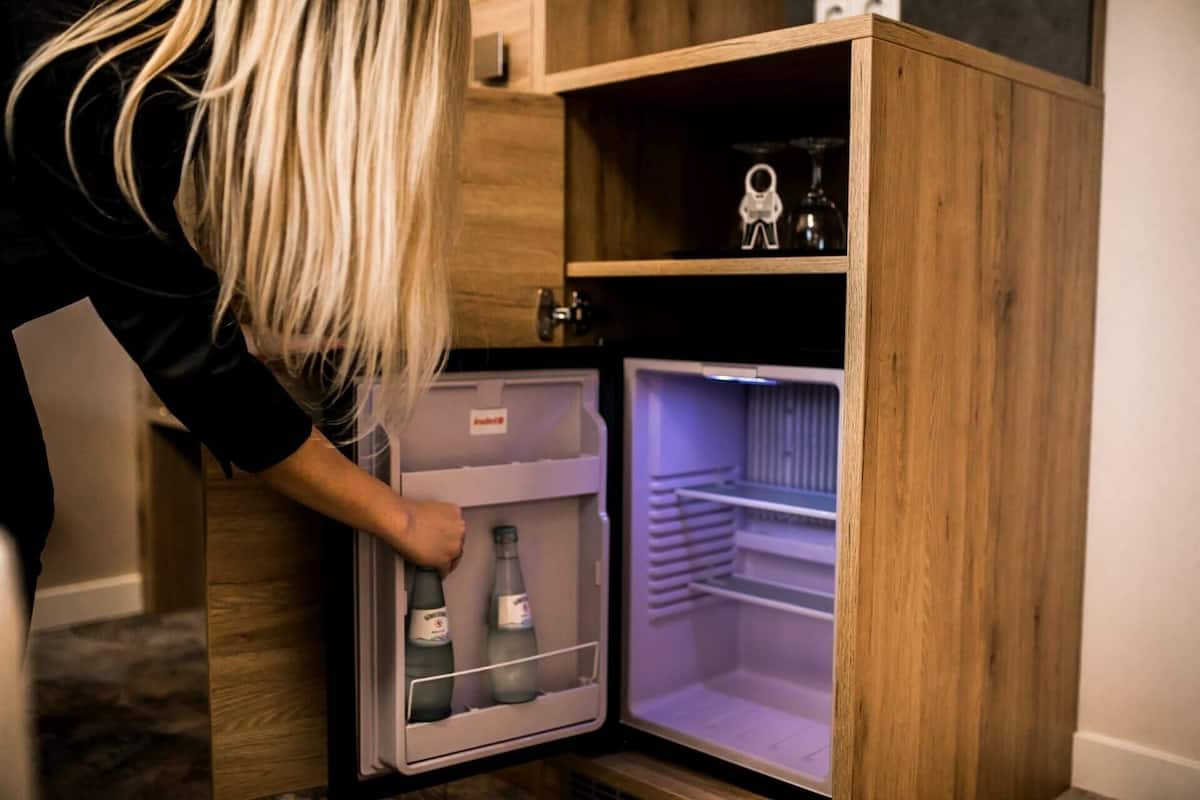 A person opening a wooden-framed refrigerator with a freezer compartment containing two bottles.