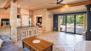 Amplia sala de estar con chimenea de piedra, una mesa de centro de madera y un amplio ventanal corredera que da a un patio exterior.