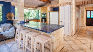 Una cocina con una isla central, taburetes de madera, paredes de piedra y vistas al exterior.