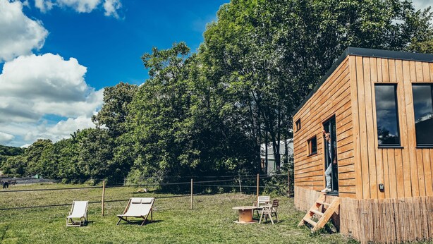Una cabaña de madera con una pequeña terraza y una mesa con sillas.