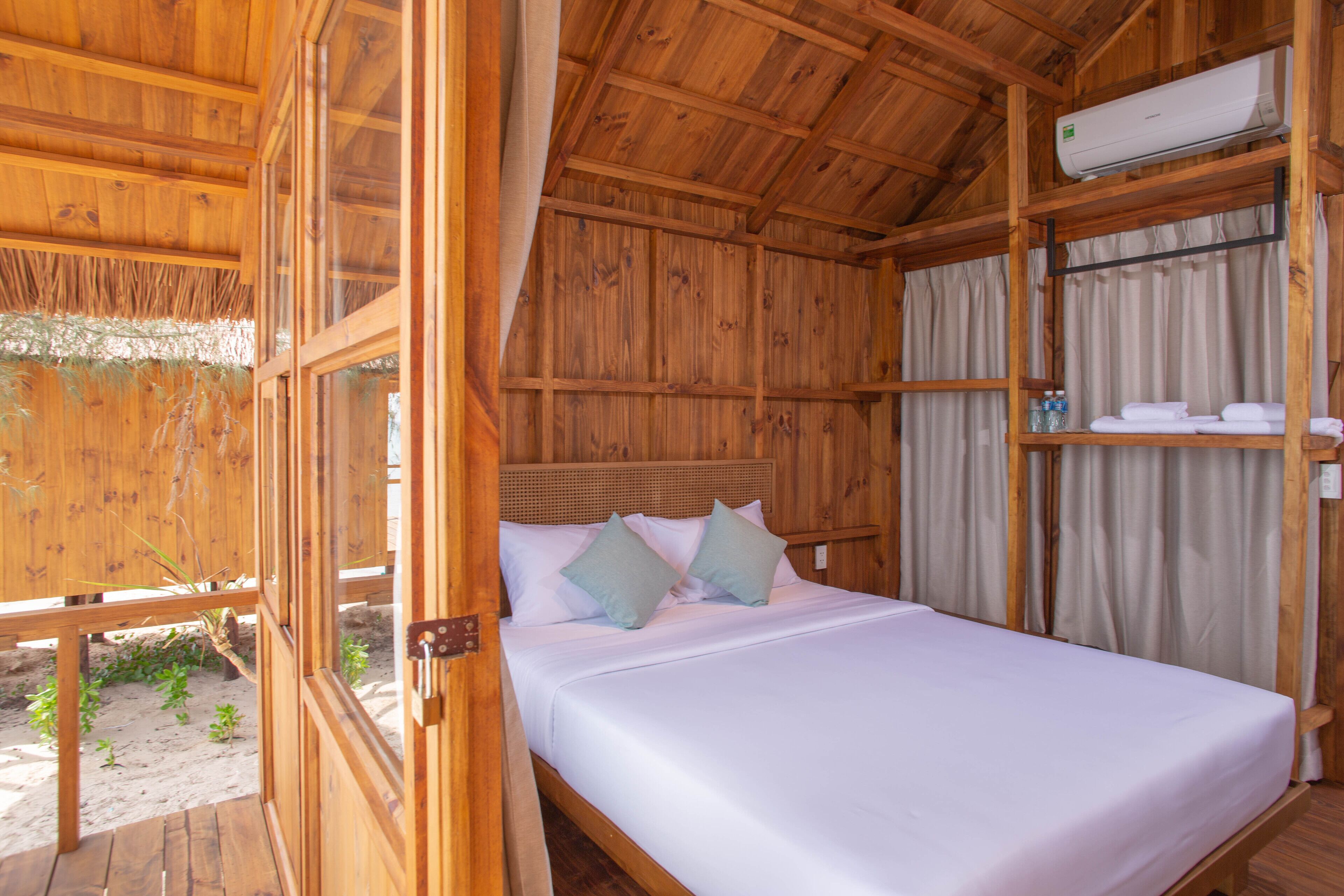 A wooden room with a bed, a shelf with towels, and an air conditioning unit.