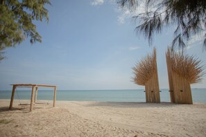 A beach with a wooden table and two thatched structures. - Hola Beach-Beach Club & Eco Glamping Resort (Tan Thanh)