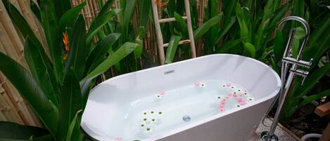 A freestanding bathtub with a bamboo backdrop, surrounded by lush green foliage.