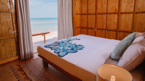 Une chambre dans un chalet en bois, avec un lit, une vue sur la plage et une fenêtre avec des rideaux.