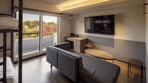 A modern hotel room with a bunk bed, a sofa, a small table, a TV, and a balcony with a view of autumn trees. - BROOKLYN HOTEL (Sapporo)