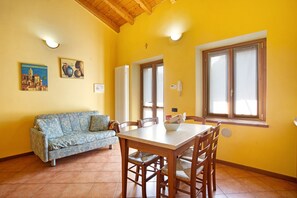 A dining area with a table and chairs, a sofa, and two paintings on the wall.