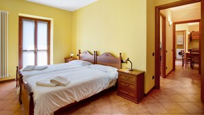 A bedroom with two beds, a wooden nightstand, a mirror, and a view of a kitchen area. - 'Residence Appartamento Roma' with Mountain View, Terrace & Wi-Fi (Civate)