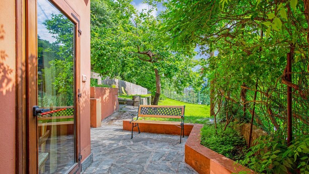 A stone pathway leading to a bench in a lush garden area with a wooden door and a window. - 'Residence Appartamento Roma' with Mountain View, Terrace & Wi-Fi (Civate)