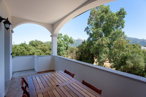 A covered outdoor seating area with a table and chairs, overlooking a mountainous landscape.