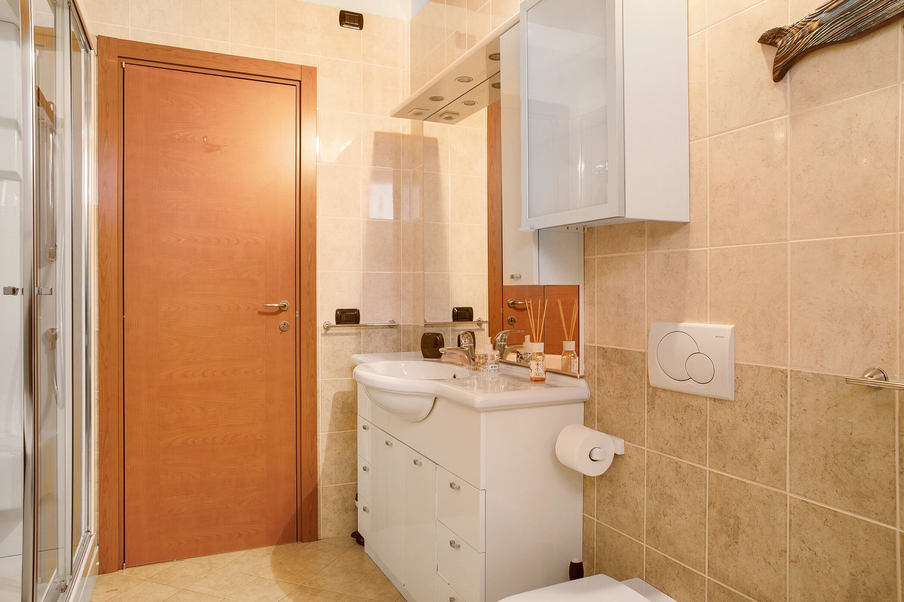 A bathroom with a wooden door, a white sink with a mirror above it, and a towel hanging on the wall.