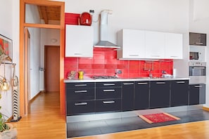 A modern kitchen with black cabinets, a red backsplash, and a wooden floor.