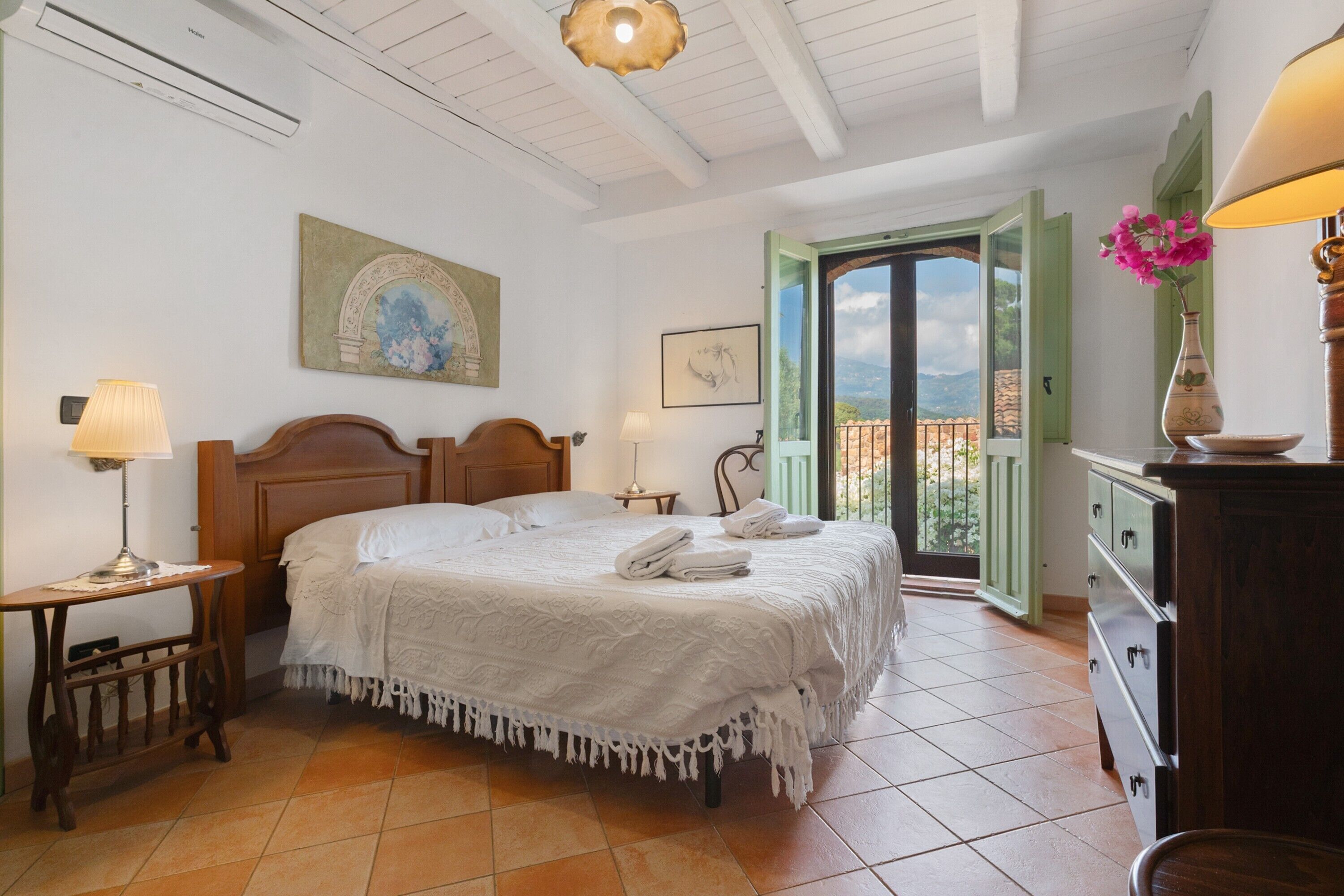 Slaapkamer met een bed, nachtkastjes, een dressoir, een schilderij, een raam met uitzicht en een openslaande deur naar een balkon.