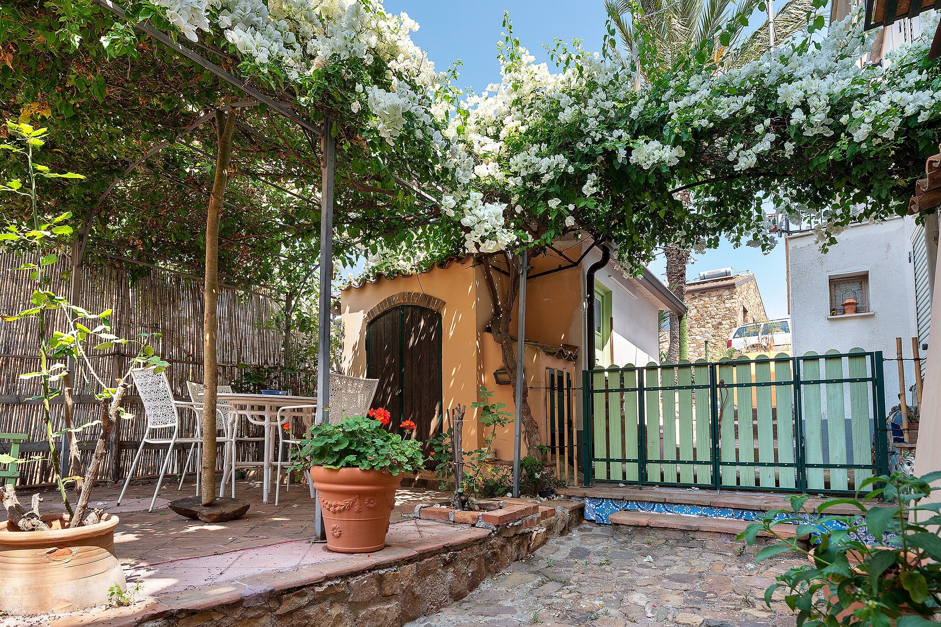 Un patio con una mesa, sillas, una planta en maceta y una cerca verde.