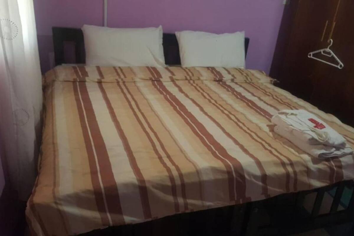 Una cama con una colcha a rayas, una almohada blanca y una prenda blanca doblada sobre la cama.