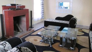 A living room with a fireplace, a flat-screen TV mounted on the wall, a patterned rug, and a black sofa.