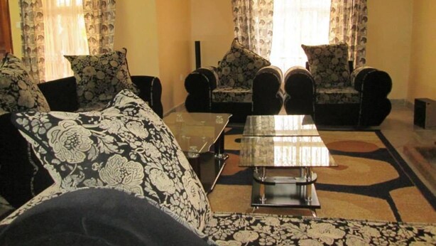 A living room with patterned sofas, a glass coffee table, and curtains.