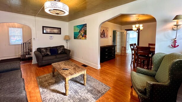 A living room with a sofa, coffee table, and chairs, wooden floors, a staircase, and a dining area with a table and chairs. - New Your Home Away From Home! - Near Great Lakes Naval Base!! (North Chicago)