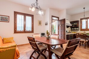 A dining area with a wooden table and chairs, a TV, and a kitchen in the background.