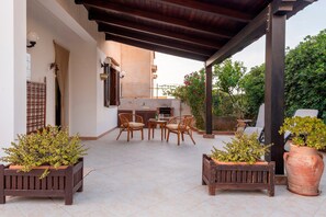 Eine Terrasse im Freien mit Holztisch und -stühlen, Blumentöpfen und einer Pergola.