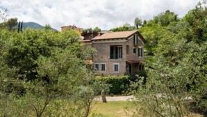 A two-story house with a tiled roof, surrounded by lush greenery and trees.