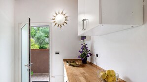 Una cocina con encimera de madera, un cuenco de limones, una planta en maceta y un adorno mural con forma de sol.