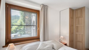 Ein Schlafzimmer mit einem Bett, einem Nachttisch mit Lampe, einem Fenster mit Jalousien und einem Holzschrank.