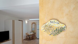 Ein Zimmer mit einem Fernseher auf einem Schrank, einem Essbereich mit Stühlen und einem Tisch, und einem Wandkunstwerk mit dem Wort 'Salvia'.