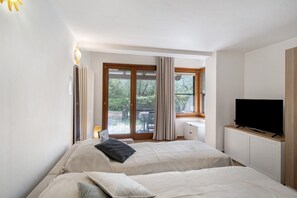 Une chambre avec deux lits, une télévision et une porte-fenêtre coulissante donnant sur l’extérieur.