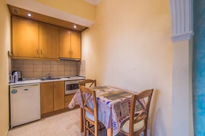 A compact kitchen with wooden cabinets, a small refrigerator, a sink, and a dining table with chairs.