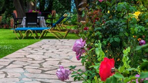A garden pathway with a stone pavement, surrounded by lush greenery and flowering plants.