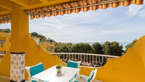 Een balkon met een witte tafel en stoelen, uitzicht op zee en gele muren.
