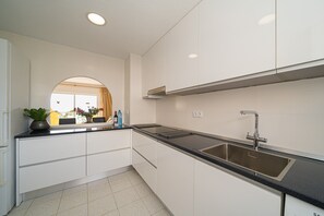 Uma cozinha moderna com armários brancos, bancada preta, pia de aço inoxidável e janela com vista.