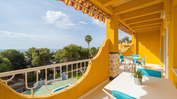 Een balkon met uitzicht op de zee, een zwembad en een eethoek met stoelen en een tafel.