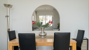 Een eetgedeelte met een houten tafel, vier zwarte stoelen, een zilveren vaas met bloemen en een hoge staande lamp.