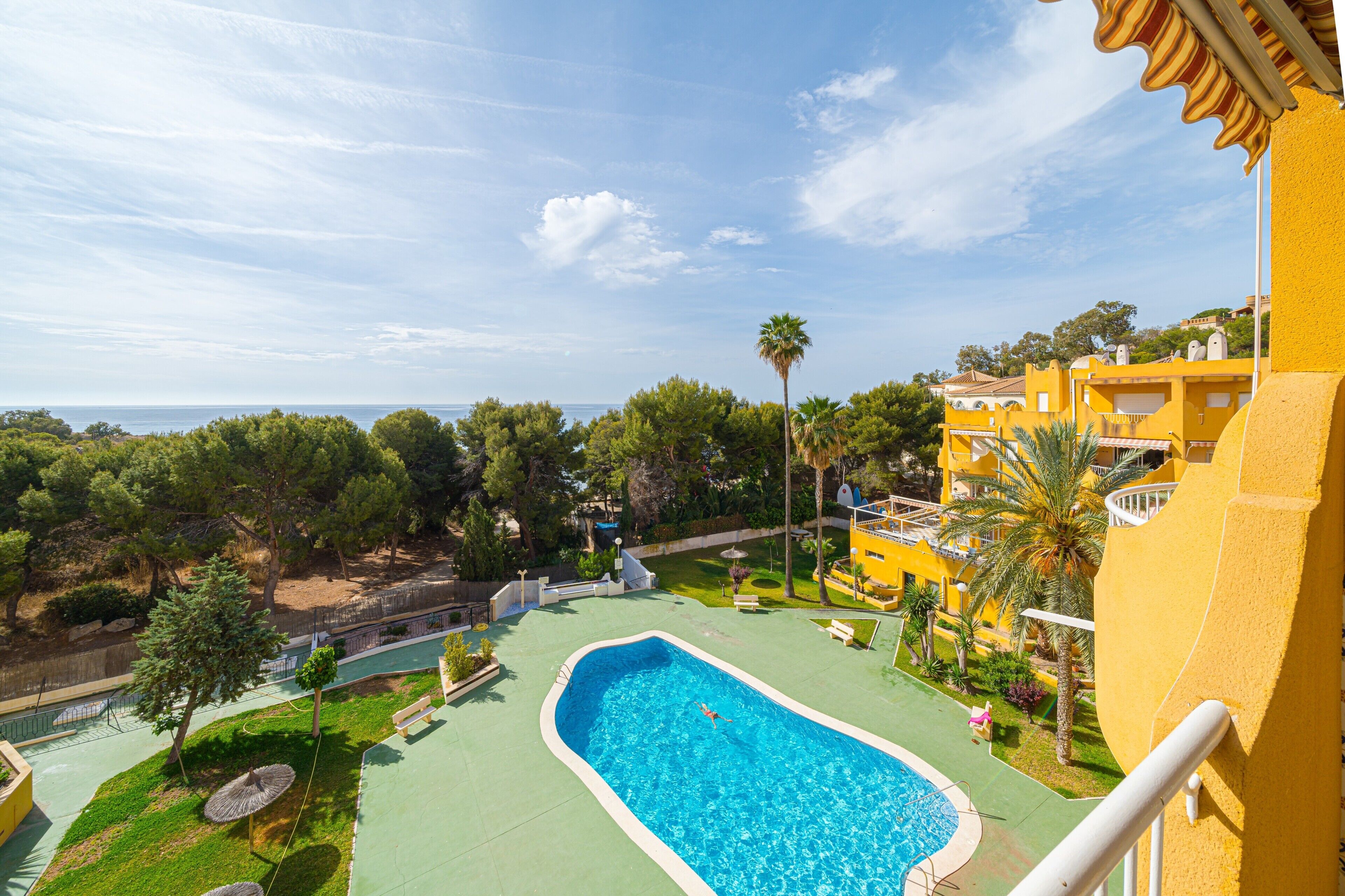Una piscina con vista sul mare, circondata da vegetazione e edifici gialli.