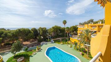 Una piscina con vista sul mare, circondata da vegetazione e edifici gialli.