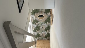 Una escala amb barana de fusta, un quadre encadrejat a la paret i un mur amb disseny a la part superior.