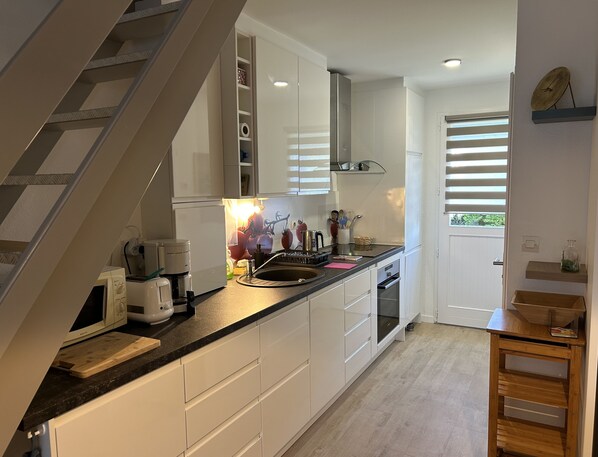 A modern kitchen with white cabinets, a black countertop, and a built-in oven. There is a wooden chair and a small wooden shelf with a glass jar.