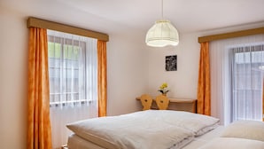 Ein Schlafzimmer mit einem Bett, zwei Nachttischen, einer Hängelampe und einem Fenster mit Vorhängen.