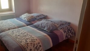 A bedroom with two beds, floral bedding, a window with curtains, and a radiator. - Apartment "Doudou Vercors" with Wi-Fi & Terrace (Lans-en-Vercors)
