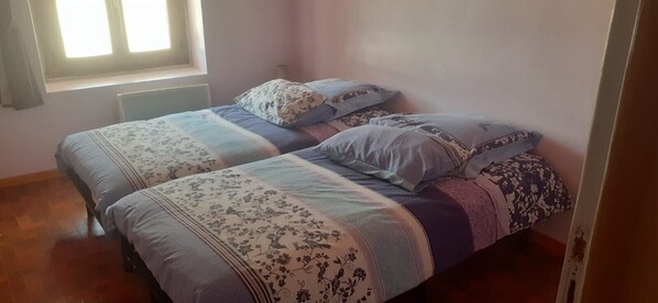 Un dormitorio con dos camas, ropa de cama floral, una ventana con cortinas y un radiador.