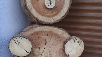 Una escultura de madera de un oso con rostro y patas, ubicada frente a una pared con fondo de lámina corrugada.