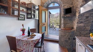 Un comedor con una mesa dispuesta para dos personas, una pared de piedra, un televisor montado en la pared y una puerta que da a un patio exterior.