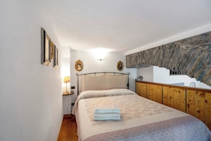 Une chambre à coucher avec un lit, une table de chevet, une lampe, des tableaux encadrés et un mur en pierre.